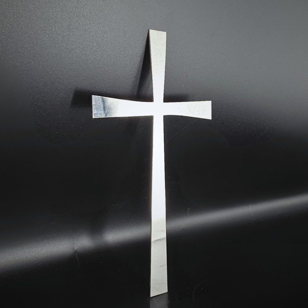 Zdjęcie przedstawia wykonany ze stali nierdzewnej krzyż wycinany laserowo.