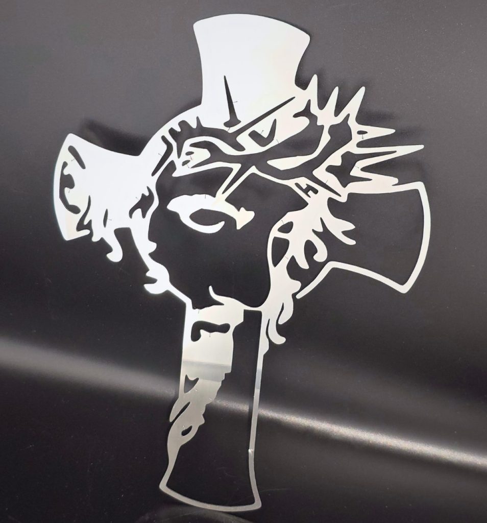 Zdjęcie przedstawia krzyż ze stali nierdzewnej z wizerunkiem Jezusa. Krzyż opiera się o czarną ścianę.