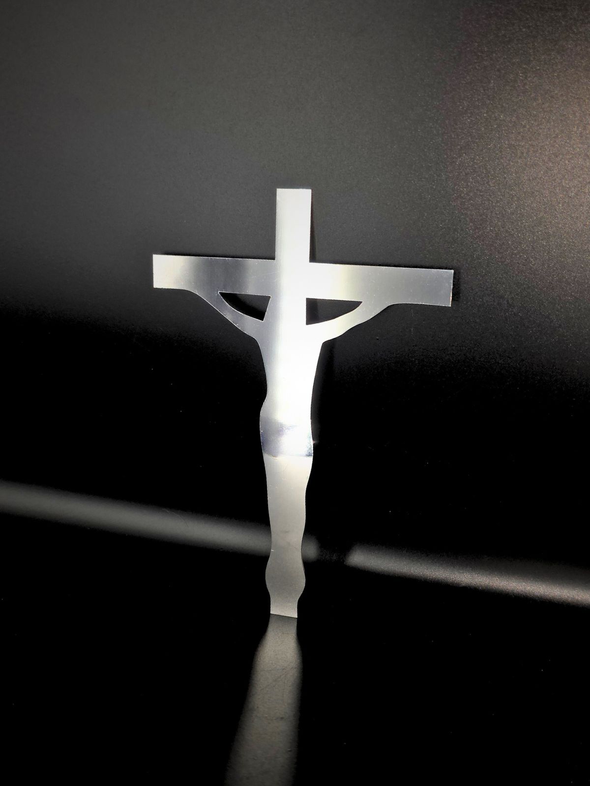 Zdjęcie przedstawia podobiznę Jezusa powieszonego na krzyżu. Jest to wykonana ze stali nierdzewnej dekoracja na grób. Opiera się o czarne tło.