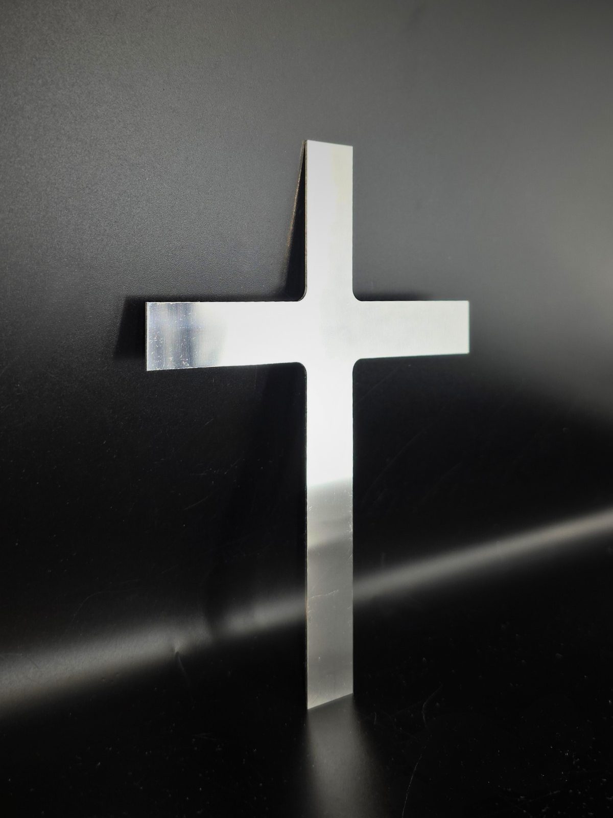 Zdjęcie przedstawia wykonany ze stali nierdzewnej krzyż oparty o czarne tło.