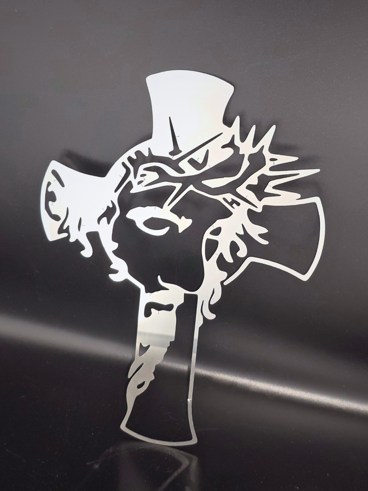 Zdjęcie przedstawia krzyż ze stali nierdzewnej z wizerunkiem Jezusa. Krzyż opiera się o czarną ścianę.